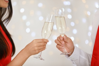 Photo of Lovely young couple with glasses of champagne against blurred festive lights, closeup. Christmas celebration