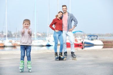 Photo of Little girl and her parents roller skating on embankment