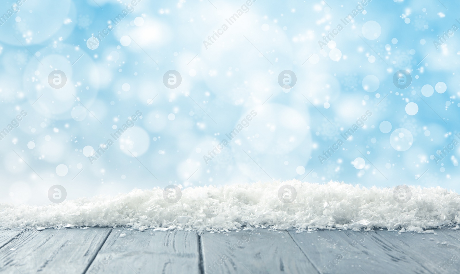 Image of Wooden surface with snow against light blue background, bokeh effect