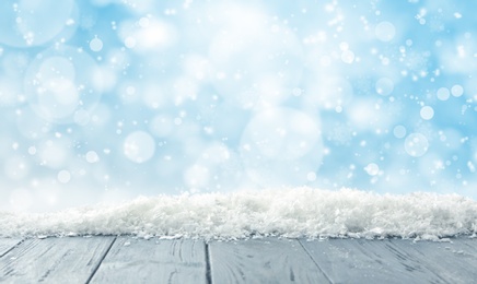 Image of Wooden surface with snow against light blue background, bokeh effect