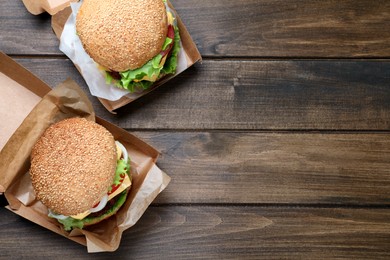 Photo of Delicious burgers in cardboard boxes on wooden table, flat lay. Space for text