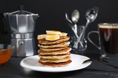 Photo of Plate of banana pancakes with honey and powdered sugar served on black table