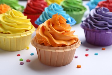 Photo of Many tasty cupcakes with bright cream and sprinkles on white background, closeup