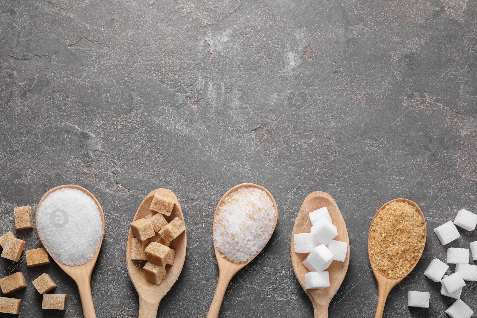 Photo of Spoons with different types of sugar on gray textured table, flat lay. Space for text