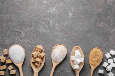 Photo of Spoons with different types of sugar on gray textured table, flat lay. Space for text