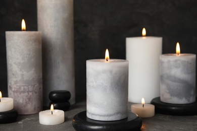 Burning candles and black spa stones on grey table