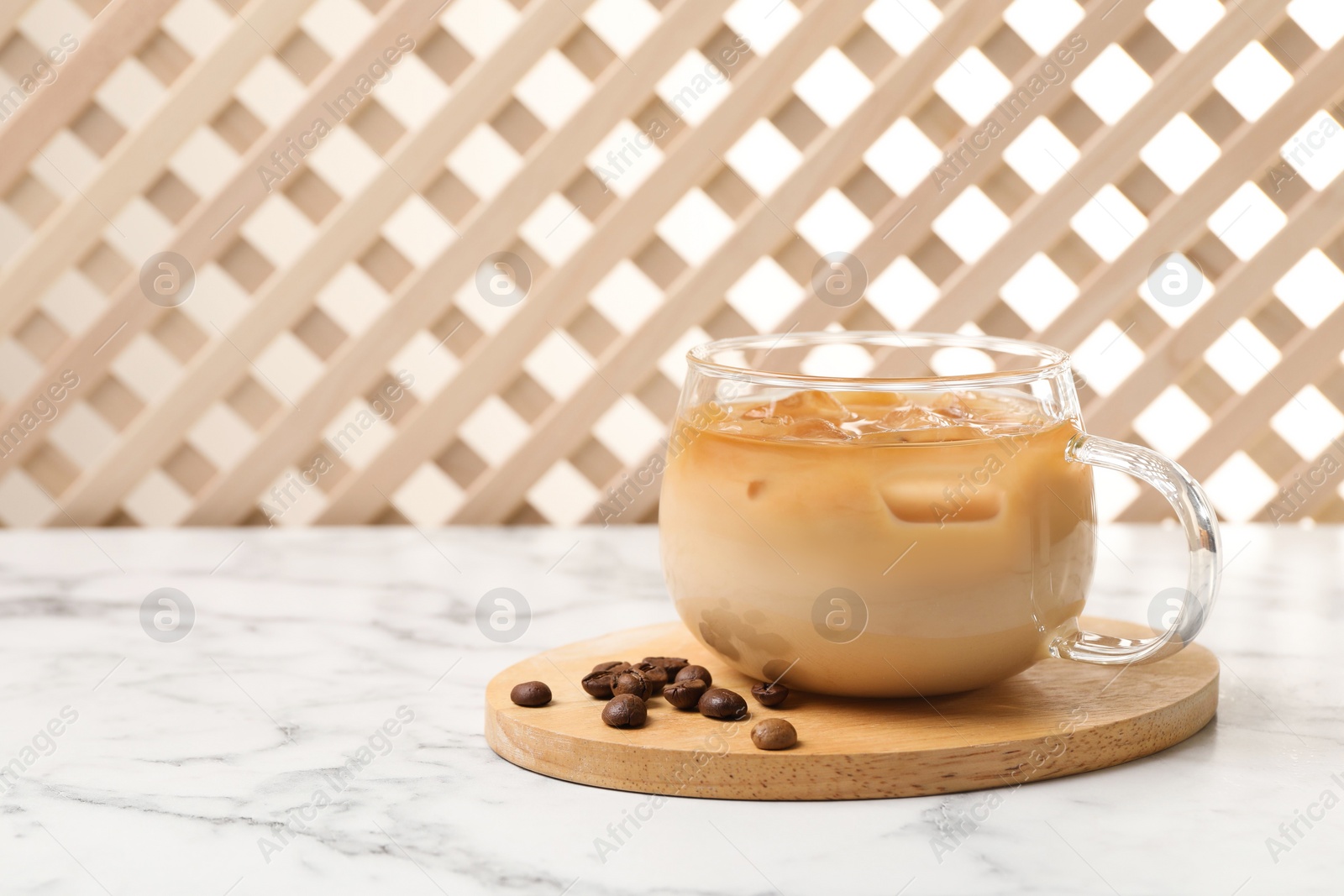 Photo of Refreshing iced coffee with milk in glass cup and beans on white marble table, space for text