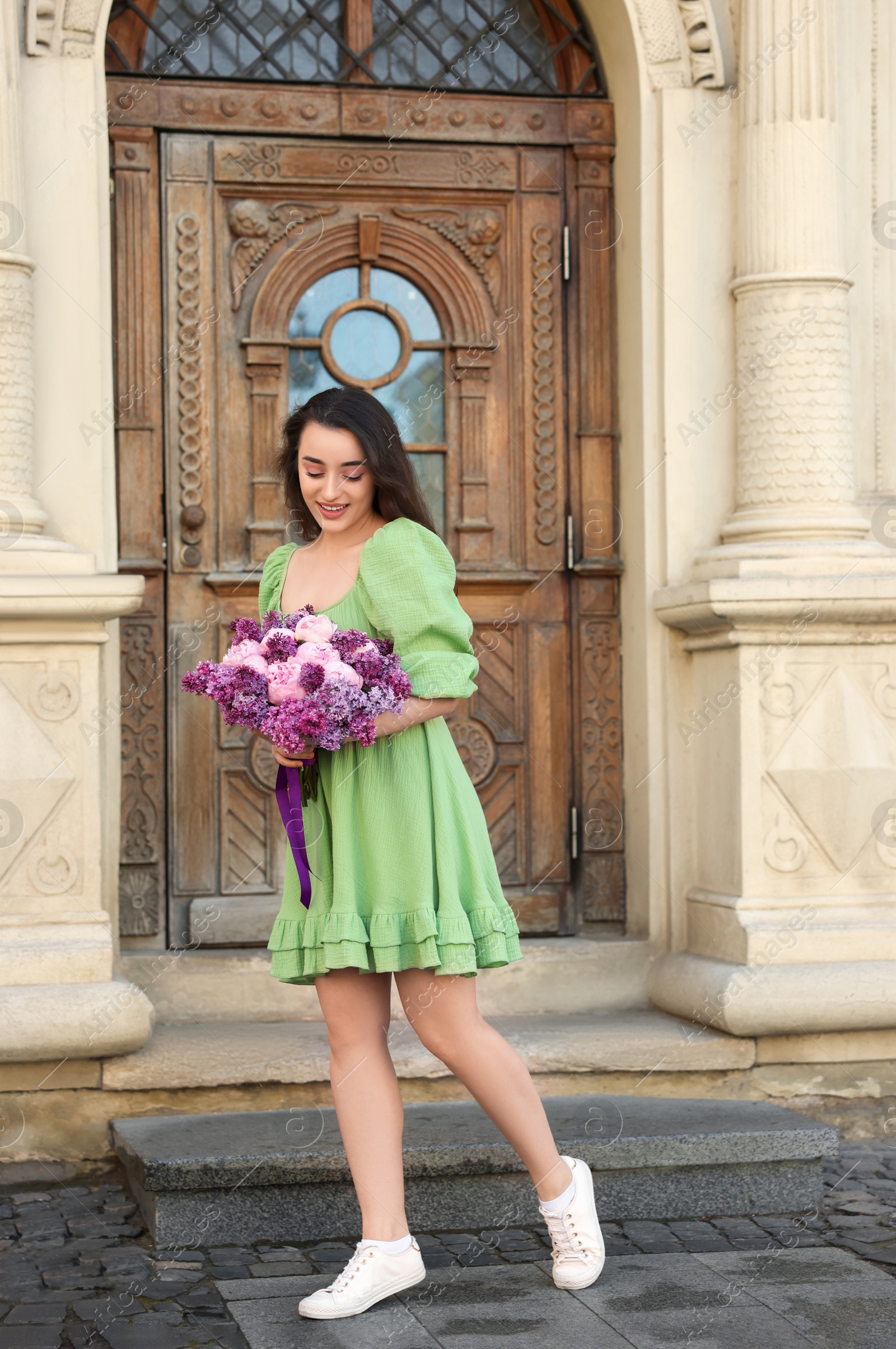 Photo of Beautiful woman with bouquet of spring flowers near building outdoors