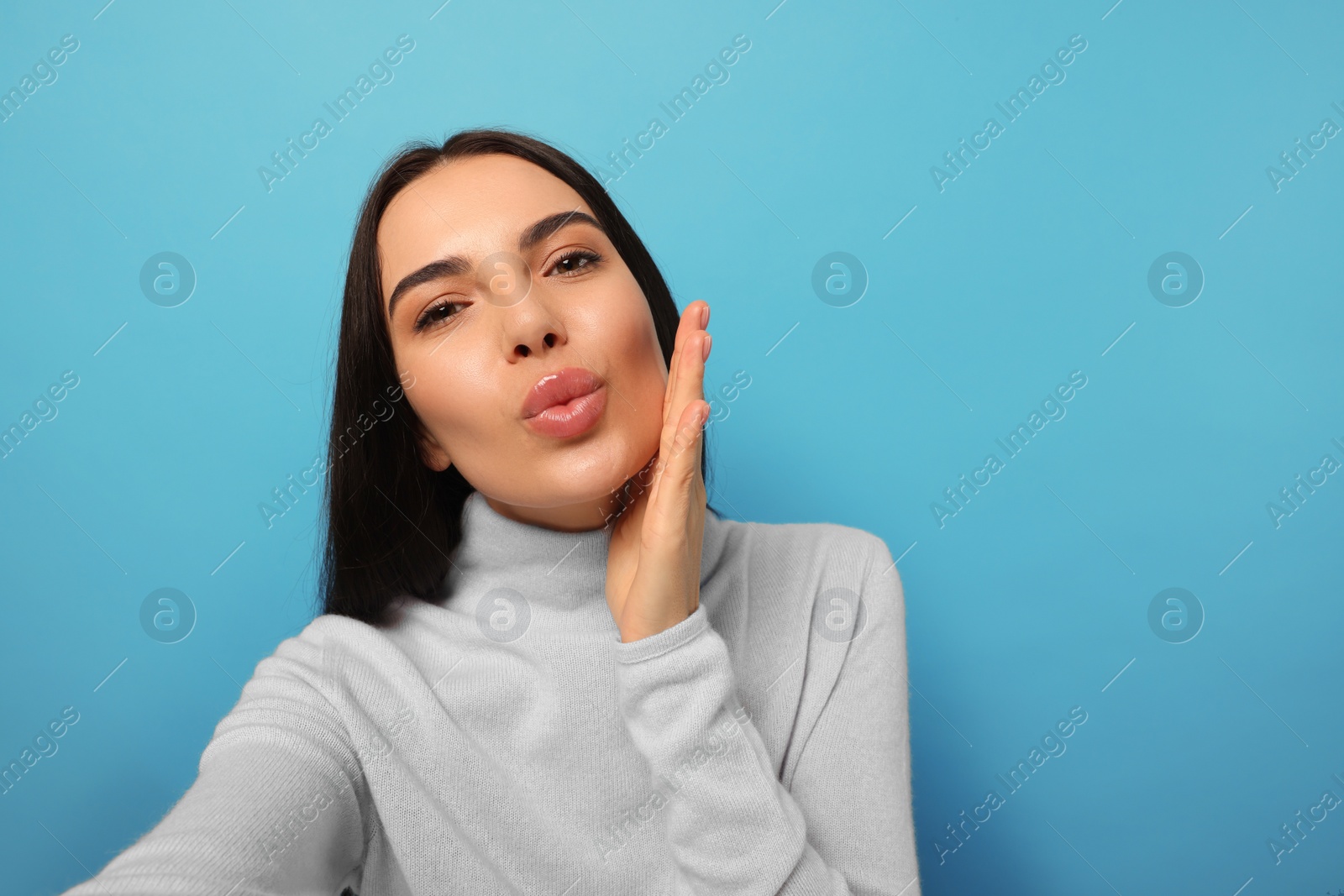 Photo of Beautiful young woman taking selfie while blowing kiss on light blue background. Space for text