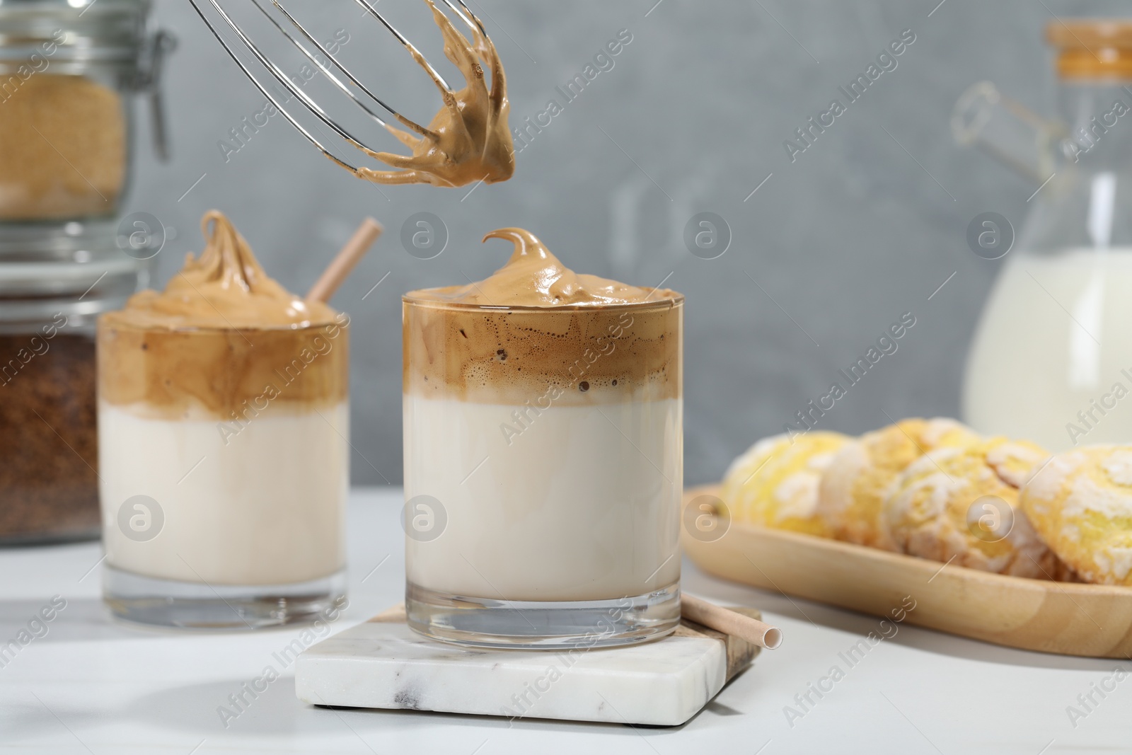 Photo of Putting cream for dalgona coffee into glass on white table, closeup