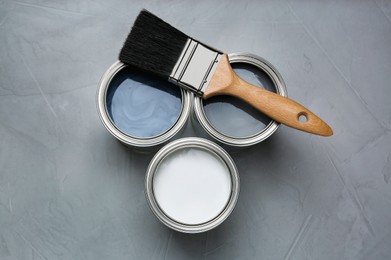 Cans with paint and brush on gray background, flat lay
