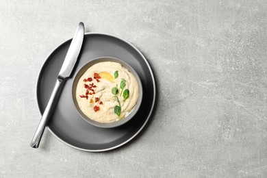 Photo of Tasty hummus with garnish in bowl served on grey table, top view. Space for text