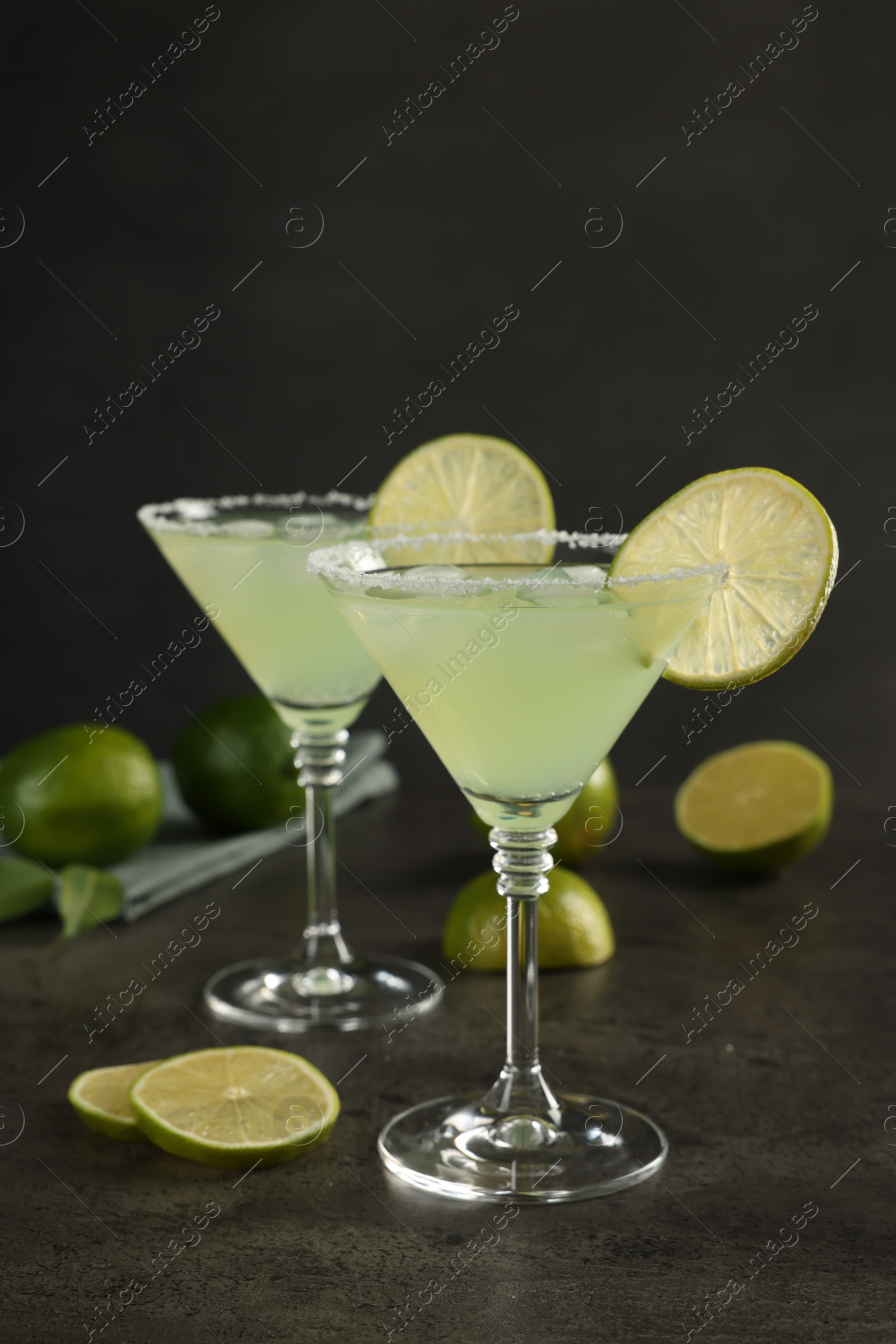 Photo of Delicious Margarita cocktail in glasses and limes on grey table