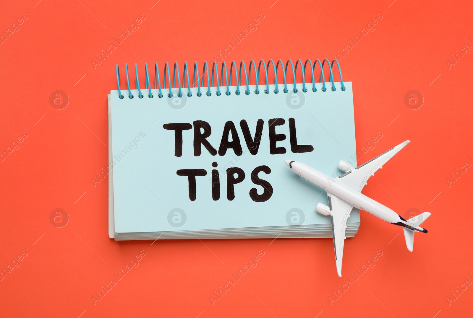 Photo of Notebook with phrase Travel Tips and toy plane on orange background, top view