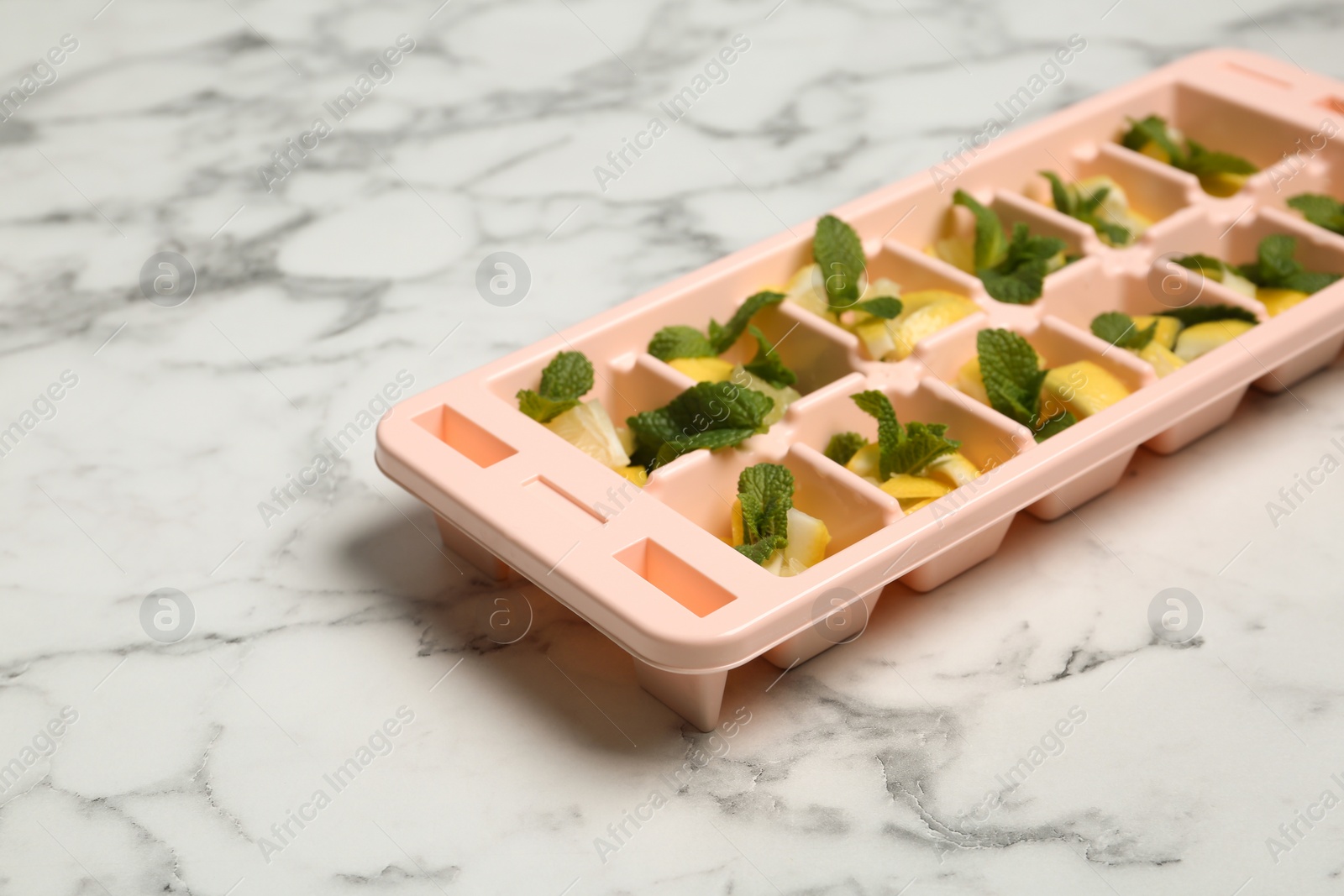 Photo of Ice cube tray with mint and lemon on marble background