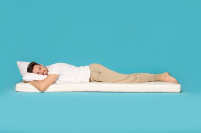 Photo of Smiling man lying on soft mattress against light blue background