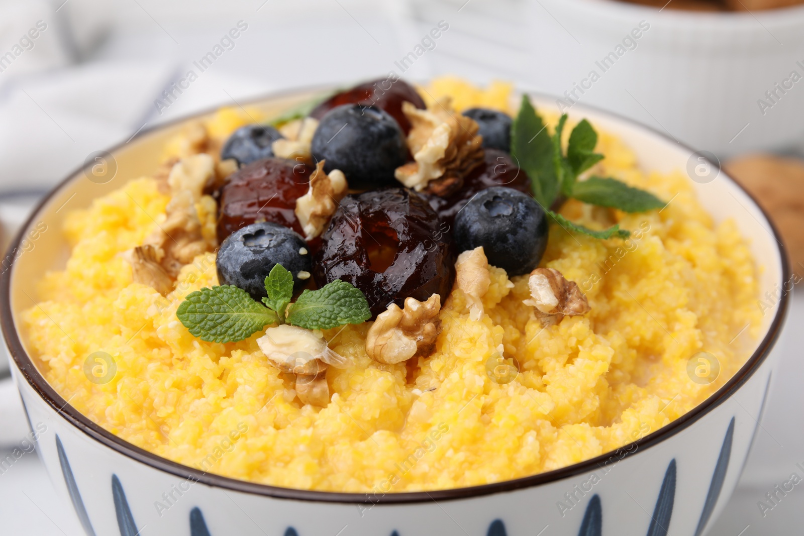 Photo of Tasty cornmeal with blueberries, dates, walnuts and mint in bowl, closeup