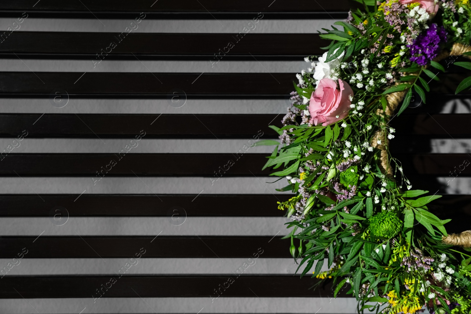 Photo of Wreath made of beautiful flowers hanging on grey wall with planks, closeup. Space for text