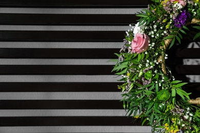 Wreath made of beautiful flowers hanging on grey wall with planks, closeup. Space for text