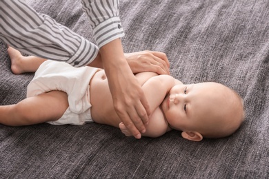 Photo of Young woman massaging cute little baby on blanket