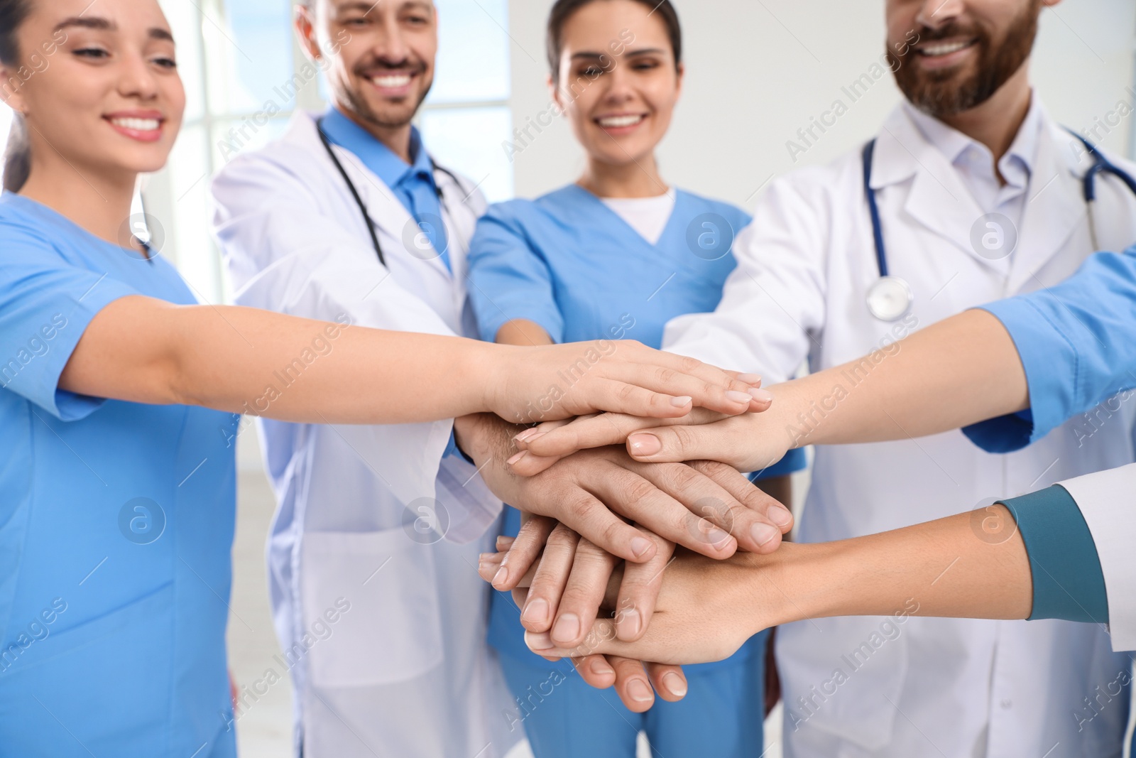 Photo of Team of medical doctors putting hands together indoors, closeup