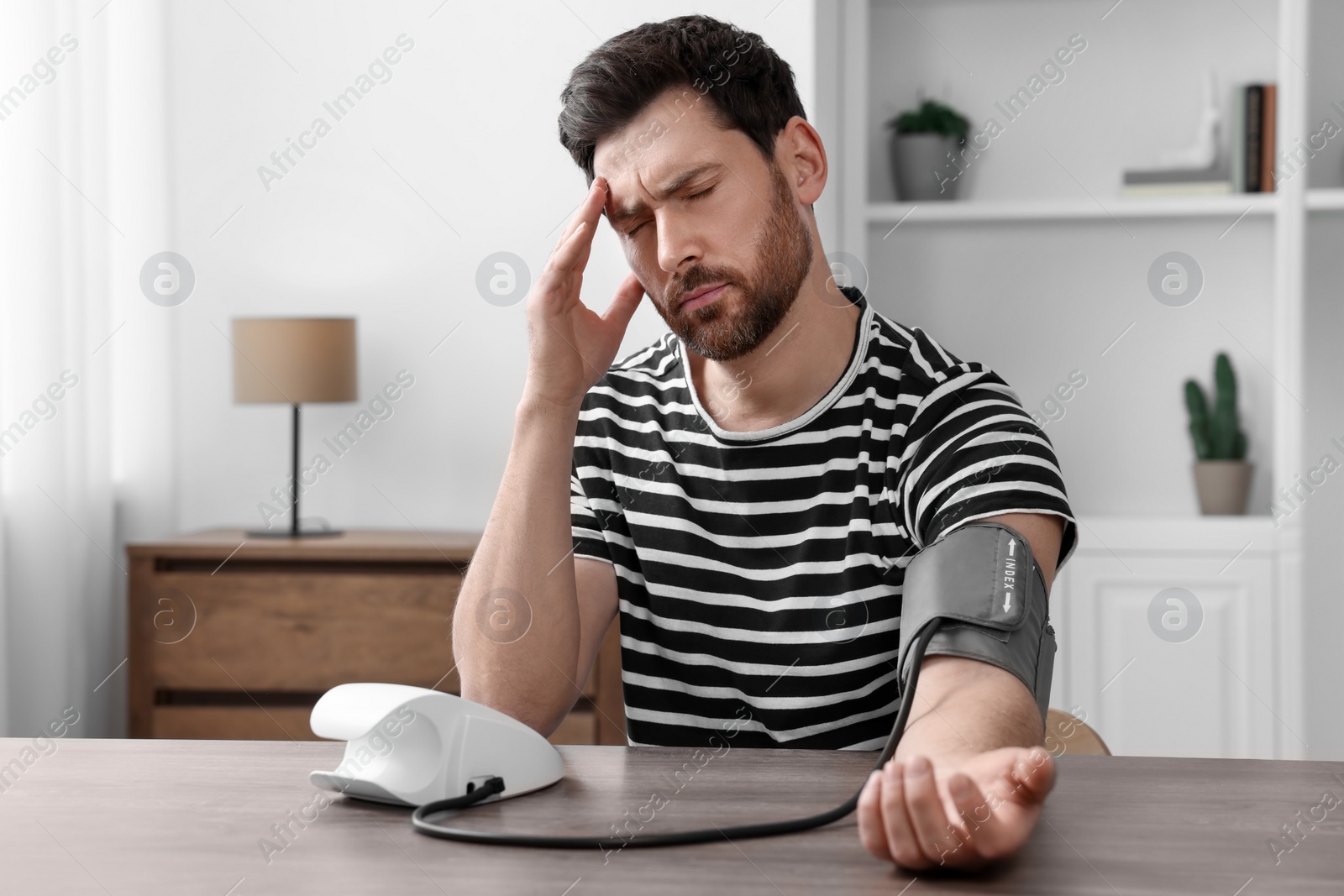 Photo of Man suffering from headache and measuring blood pressure in room