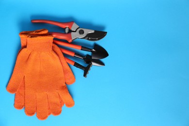 Photo of Gardening gloves and tools on light blue background, flat lay. Space for text