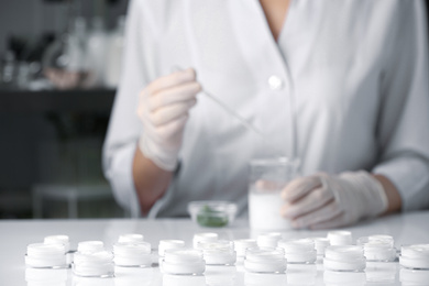 Photo of Scientist working in laboratory, focus on jars with different cosmetic products