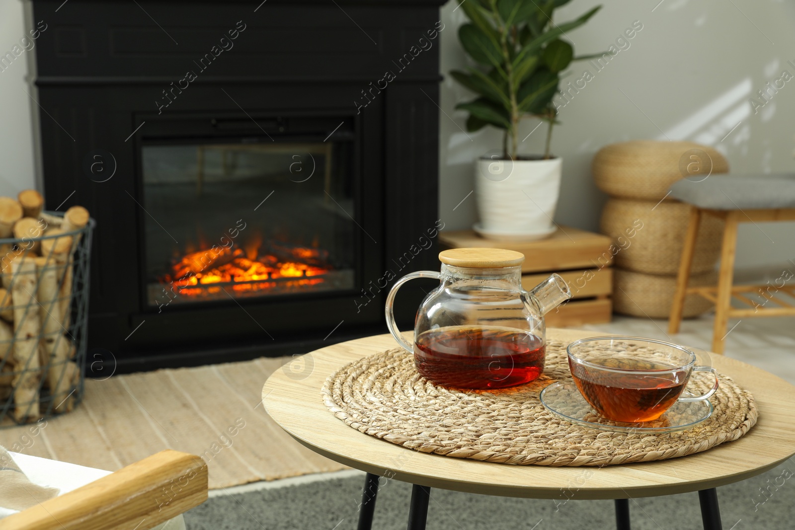 Photo of Teapot and cup of drink on coffee table near stylish fireplace in cosy living room. Interior design