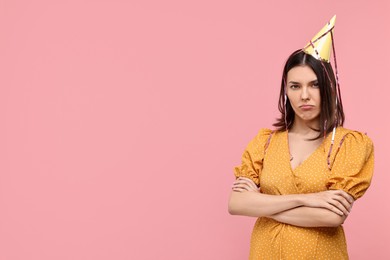 Sad young woman in party hat on pink background