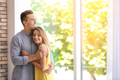 Photo of Happy young couple standing near window at home