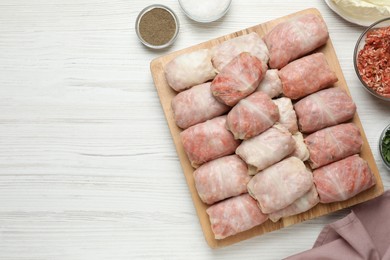 Uncooked stuffed cabbage rolls on white wooden table, flat lay. Space for text