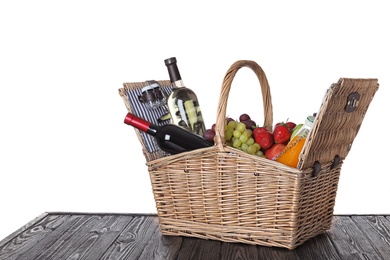 Photo of Wicker picnic basket with wine and different products on wooden table against white background, space for text