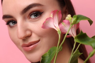 Beautiful woman with fake freckles and flowers on pink background, closeup
