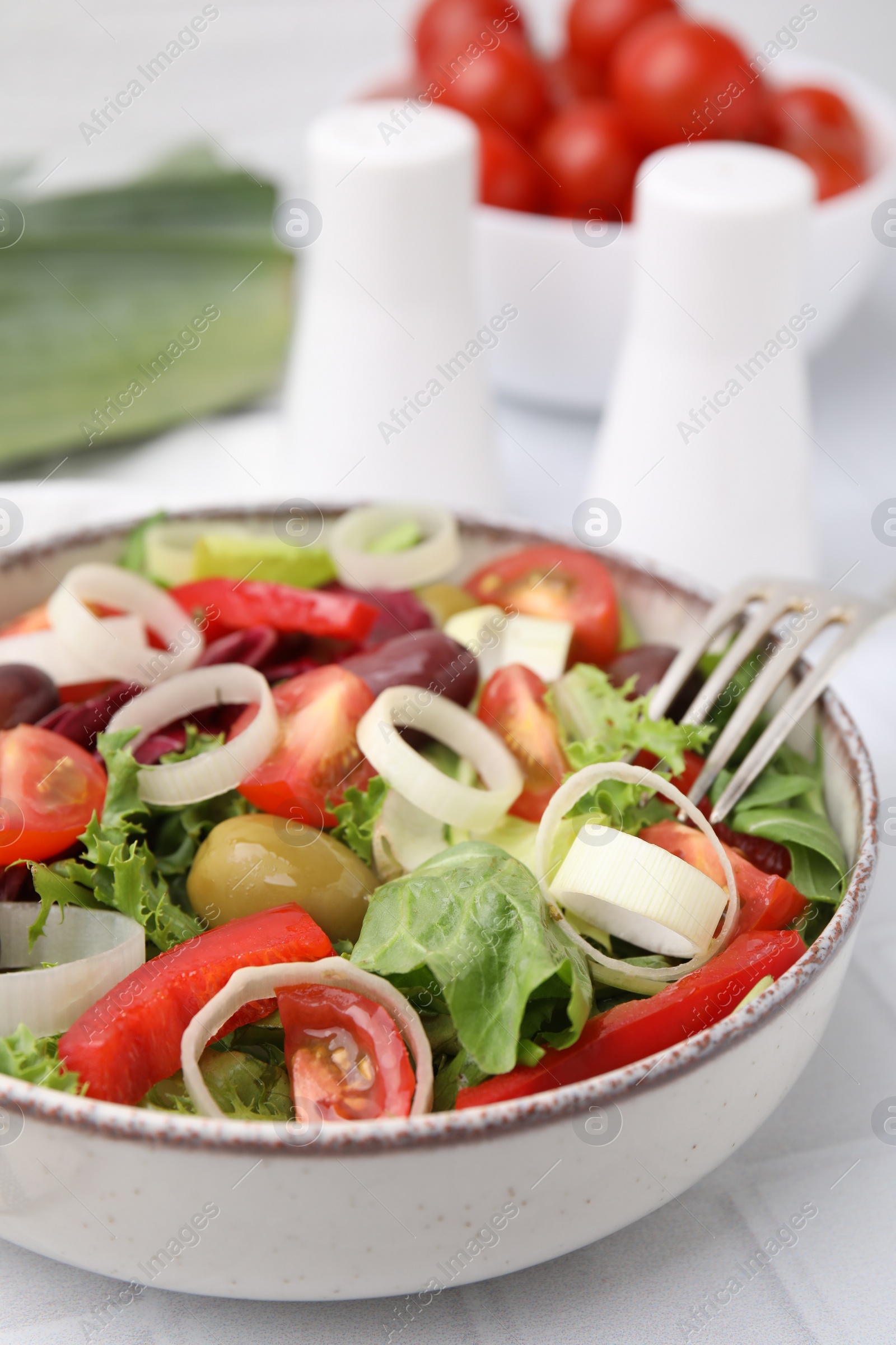Photo of Bowl of tasty salad with leek and olives on white tiled table, closeup