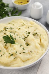 Photo of Bowl of tasty mashed potato, parsley, olive oil and pepper on grey marble table, closeup