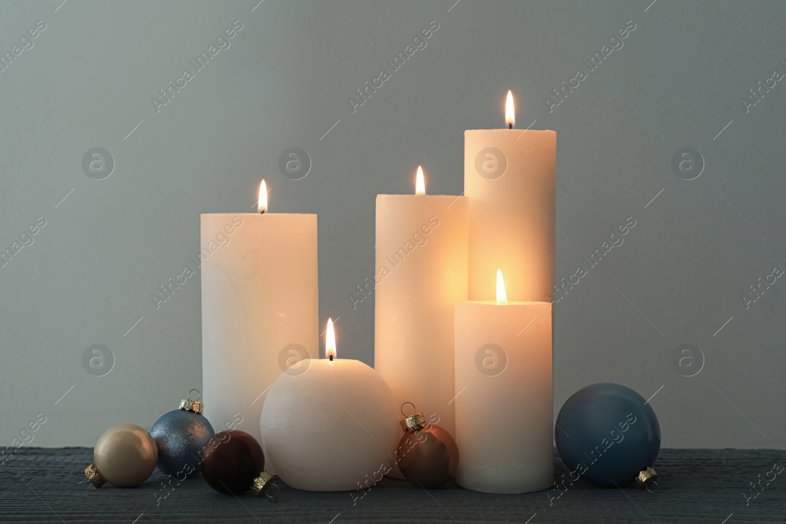 Photo of Burning candles and Christmas baubles on grey wooden table