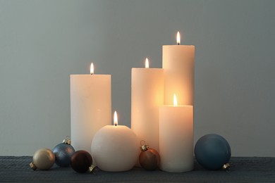 Photo of Burning candles and Christmas baubles on grey wooden table