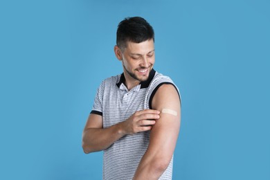 Vaccinated man with medical plaster on his arm against light blue background