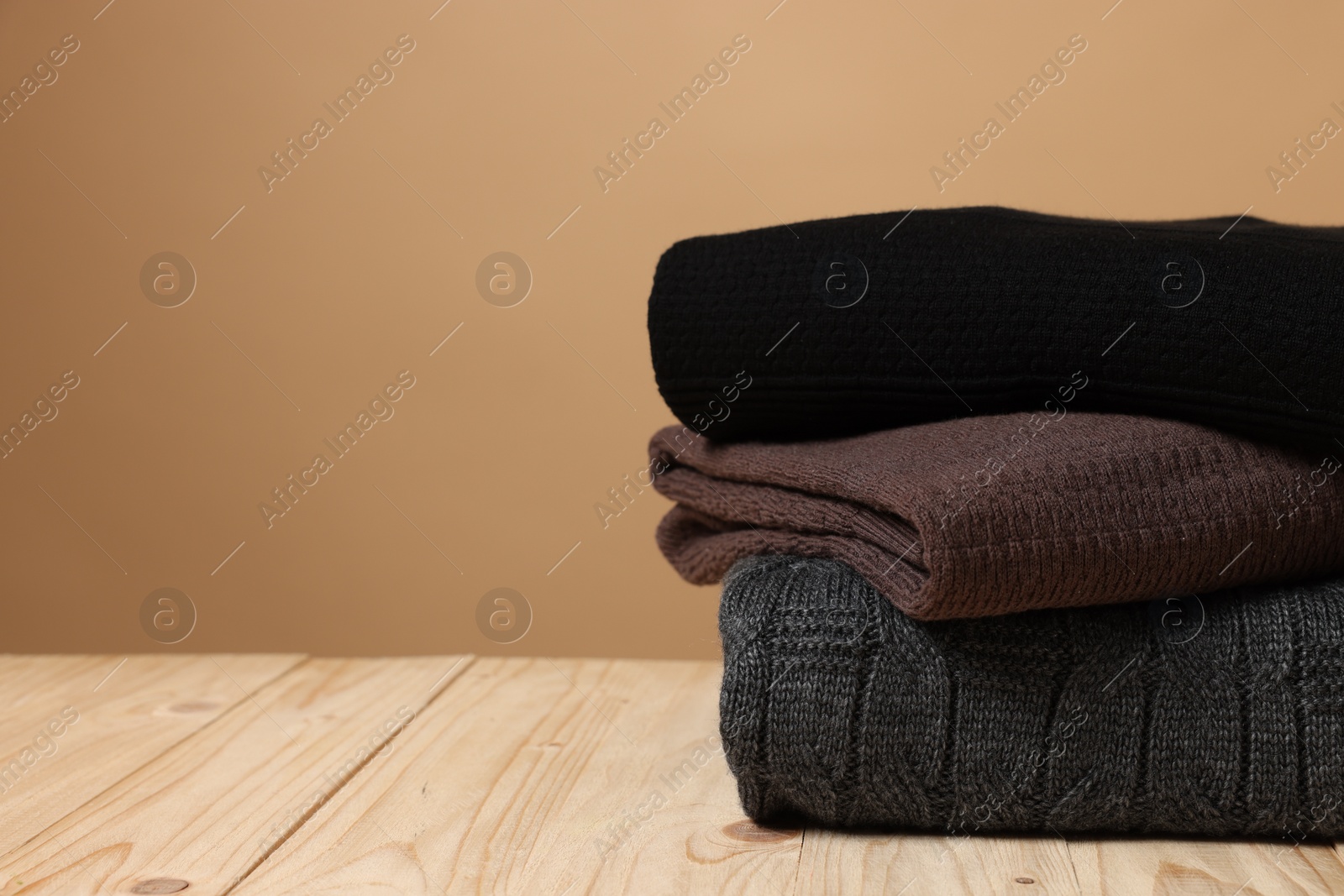 Photo of Stack of casual sweaters on wooden table against light brown background. Space for text