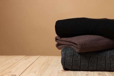 Photo of Stack of casual sweaters on wooden table against light brown background. Space for text