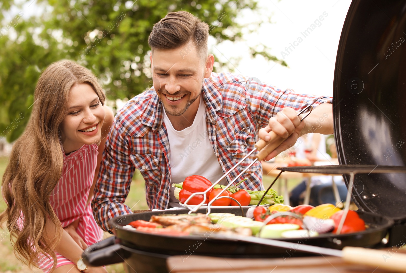 Photo of Young couple having barbecue with modern grill outdoors