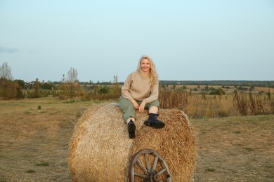 Beautiful woman sitting on hay bale in field. Autumn season