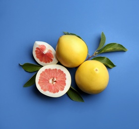 Photo of Fresh cut and whole pomelo fruits with leaves on blue background, flat lay