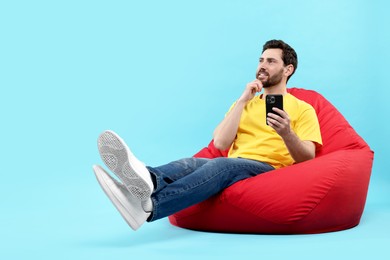 Photo of Smiling man with smartphone sitting on bean bag against light blue background. Space for text