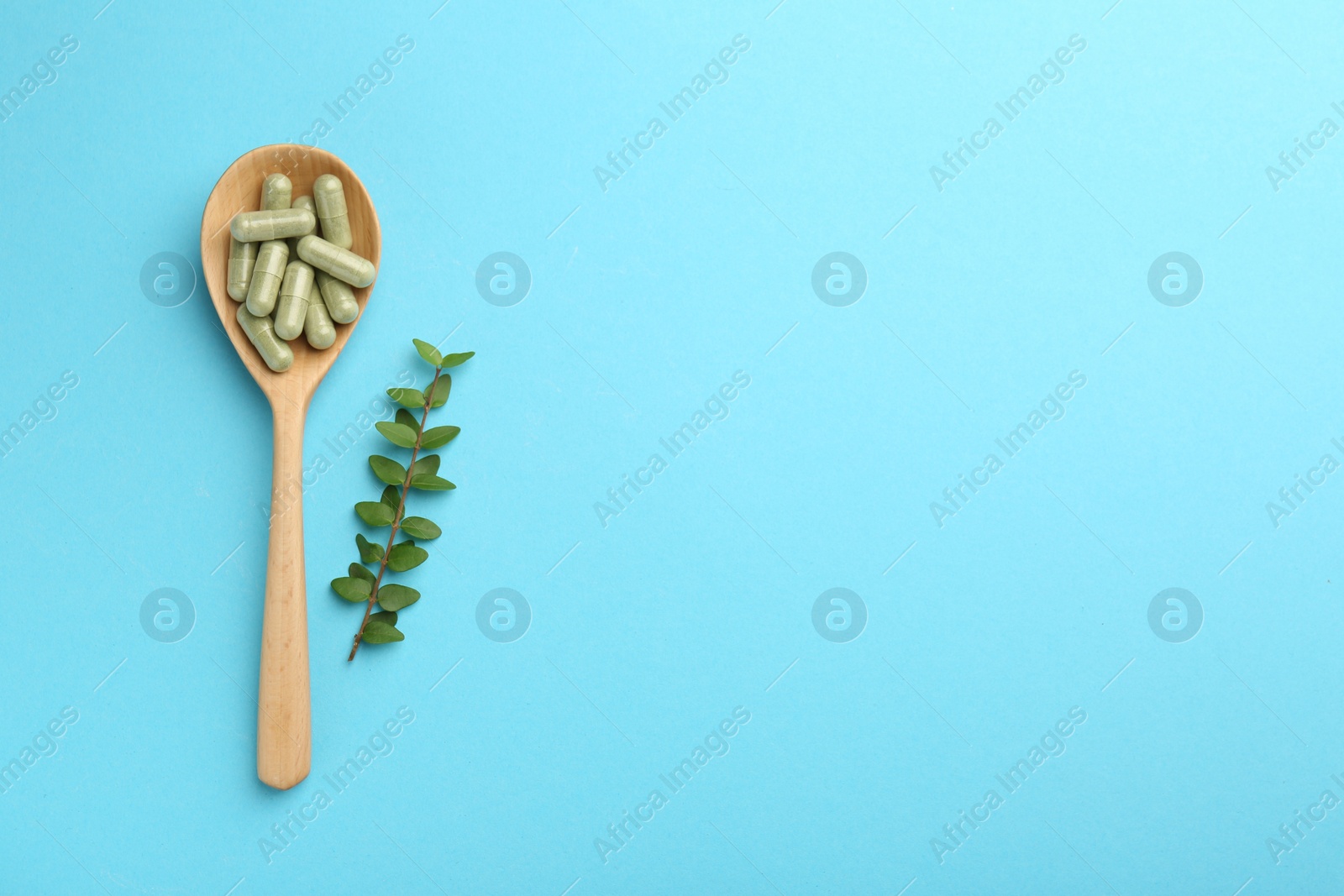 Photo of Vitamin capsules in spoon and green branch on light blue background, flat lay. Space for text