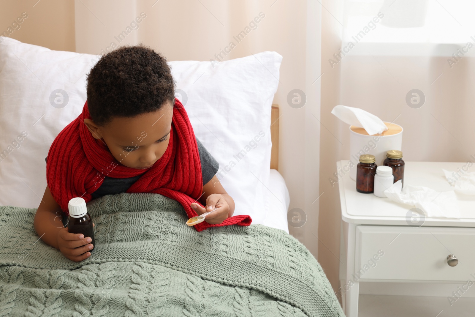 Photo of African-American boy taking cough syrup on bed at home, space for text. Cold medicine