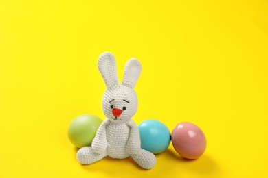 Cute Easter bunny toy and dyed eggs on color background