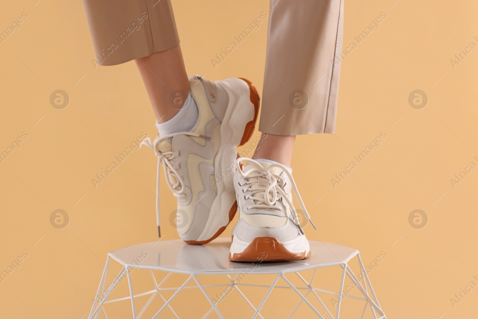 Photo of Woman in stylish new sneakers standing on white table against beige background, closeup