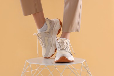 Woman in stylish new sneakers standing on white table against beige background, closeup